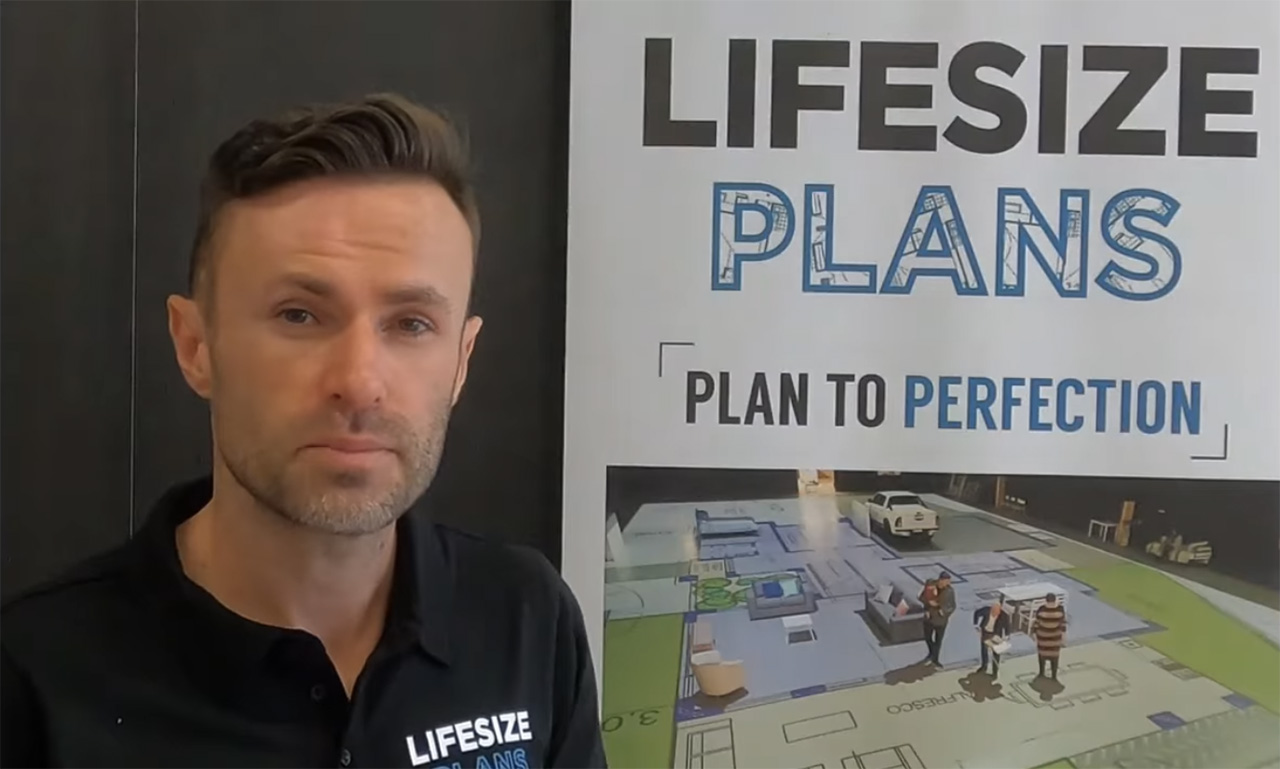 A man stands in front of a sign that reads "life size plans".